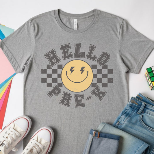 Hello Pre-K back-to-school design featuring distressed collegiate lettering, a yellow smiley face with lightning-bolt eyes, and bold black checkerboard accents for preschool shirts.