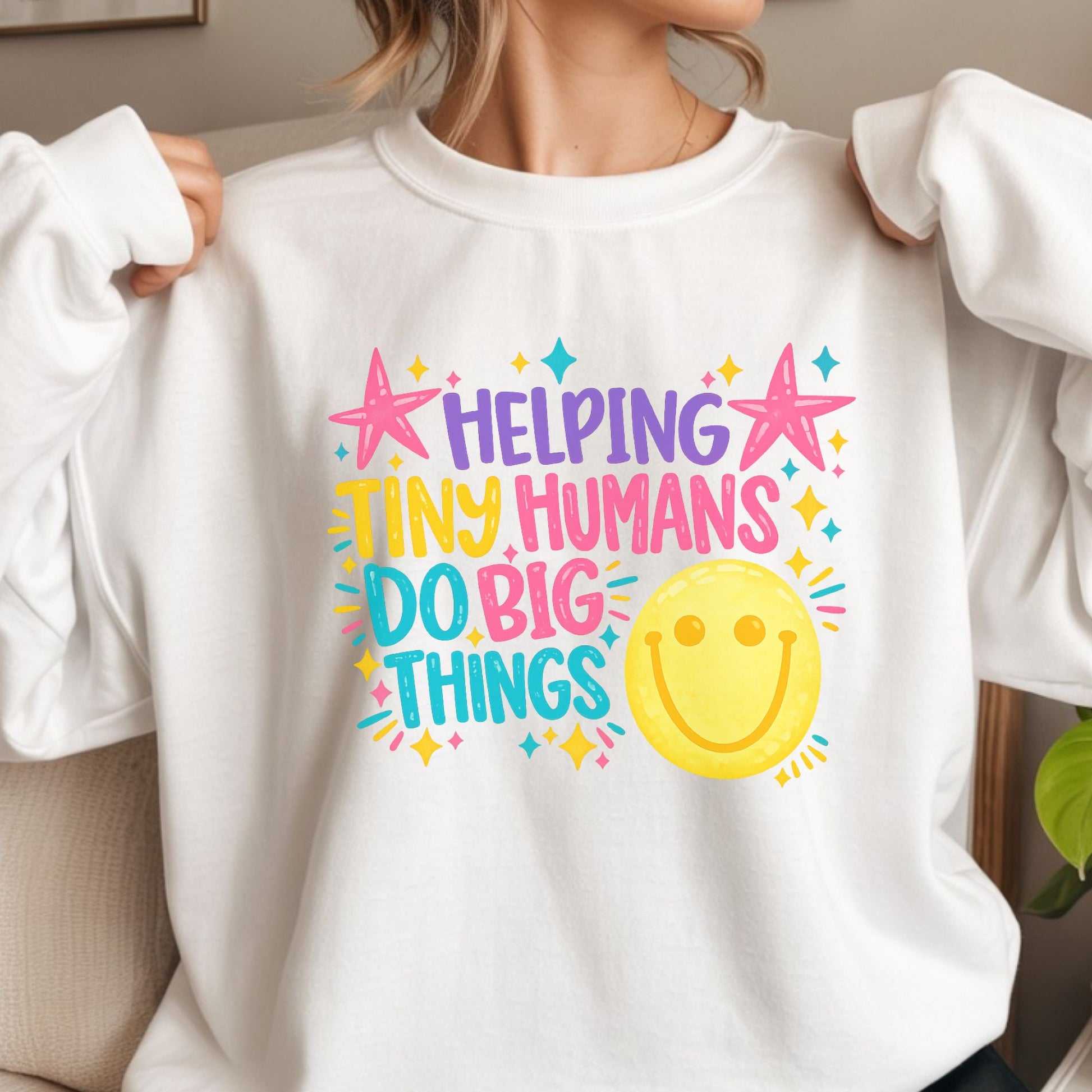 Helping Tiny Humans Do Big Things teacher design featuring bright pink, purple, yellow, and teal lettering with stars, sparkles, and a large cheerful smiley face for colorful classroom apparel.