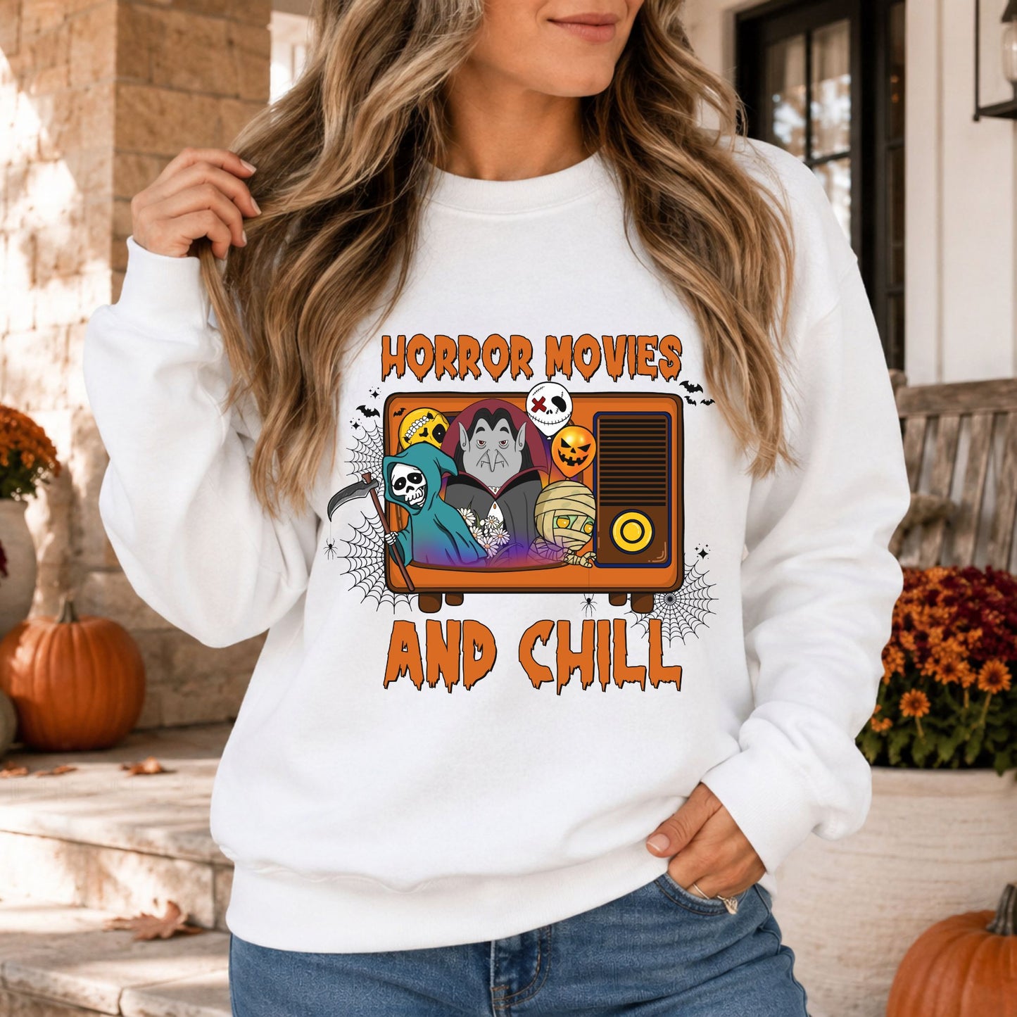 Colorful Horror Movies and Chill Halloween DTF transfer featuring a retro television filled with a grim reaper, vampire, mummy, jack-o-lantern and skull characters, surrounded by spiderwebs, spiders and bats on a white sweatshirt mockup.