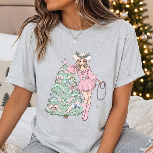 Cowgirl in a pink dress, white cowboy hat and pink boots holding a lasso beside a mint green Christmas tree decorated with pastel bows, hearts and ribbons.