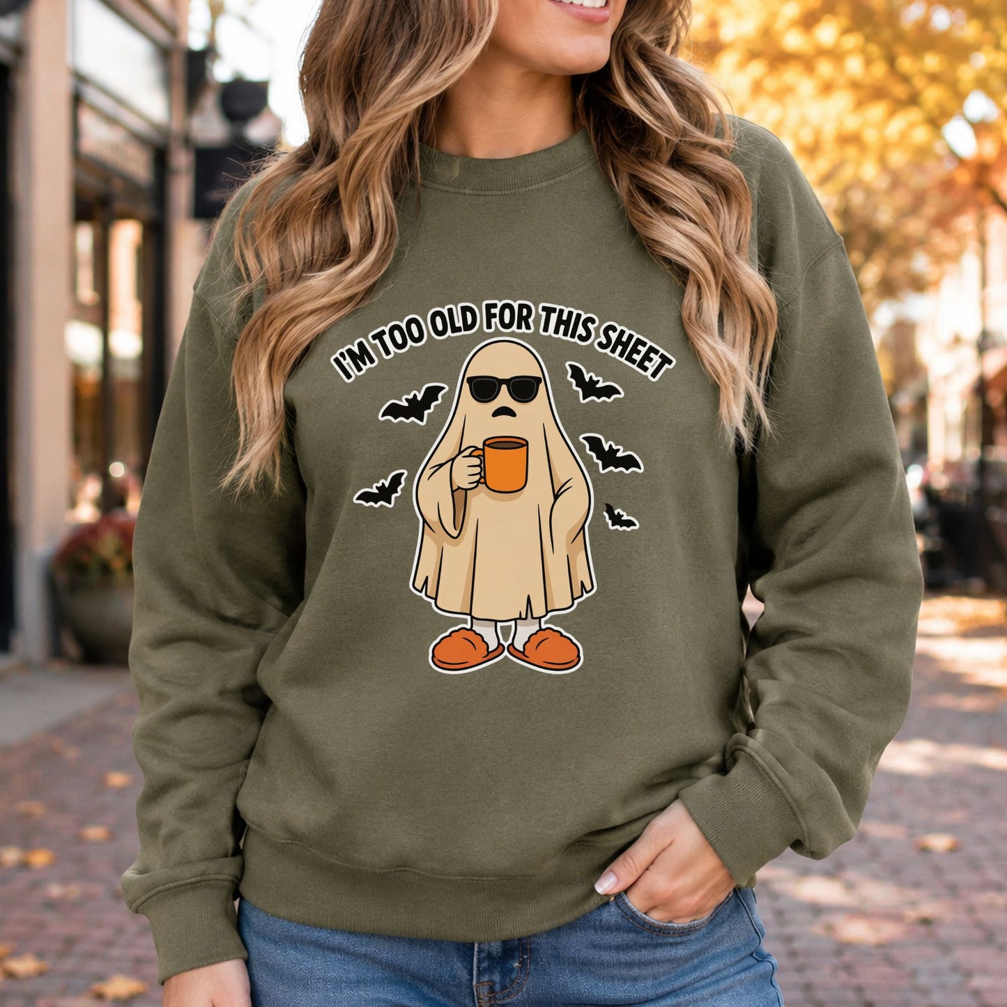 I’m Too Old for This Sheet Halloween DTF transfer featuring a tired sheet ghost wearing black sunglasses and orange slippers while holding a coffee mug, surrounded by flying bats on an olive green sweatshirt mockup.