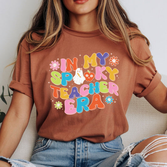 In My Spooky Teacher Era design featuring colorful retro bubble lettering, a cute ghost, apple, skull flowers, sparkles, and playful Halloween teacher style.