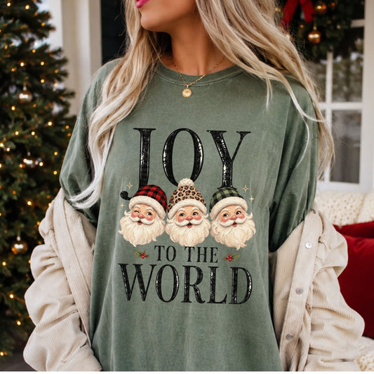 “Joy to the World” in distressed black lettering with three vintage Santa faces wearing red plaid, leopard print and green plaid hats, accented by holly and gold stars.