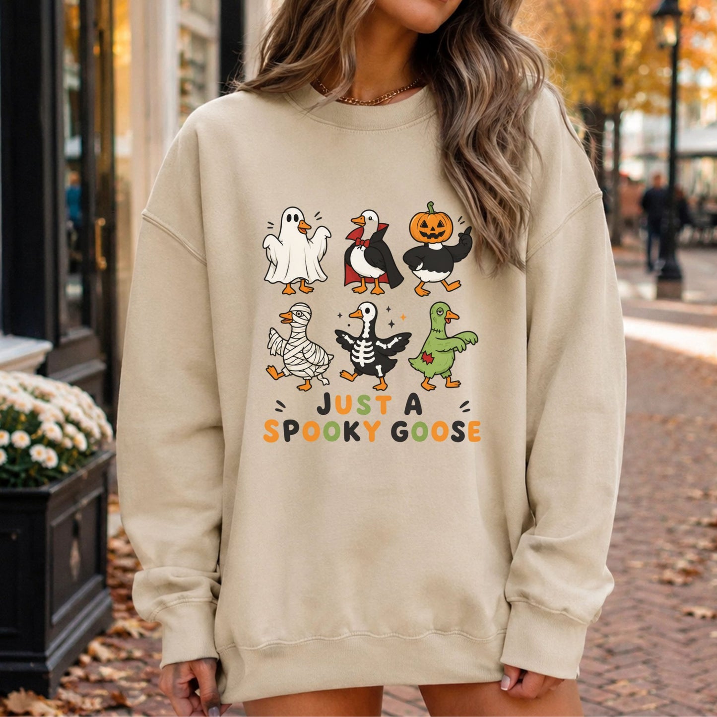 Just a Spooky Goose Halloween DTF transfer featuring six playful geese dressed in ghost, vampire, jack-o’-lantern, mummy, skeleton and zombie costumes, arranged in two rows above orange and black lettering on a cream sweatshirt mockup.