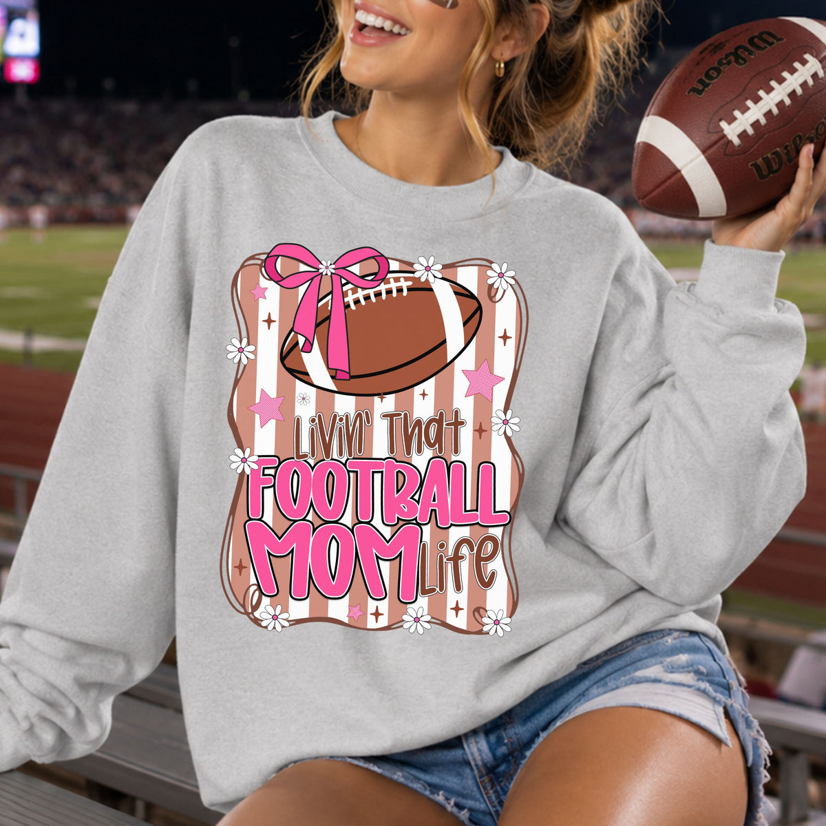 Livin’ That Football Mom Life DTF transfer featuring a brown football with a bright pink bow, retro brown and white stripes, pink stars, daisies, and bold pink Football Mom lettering.