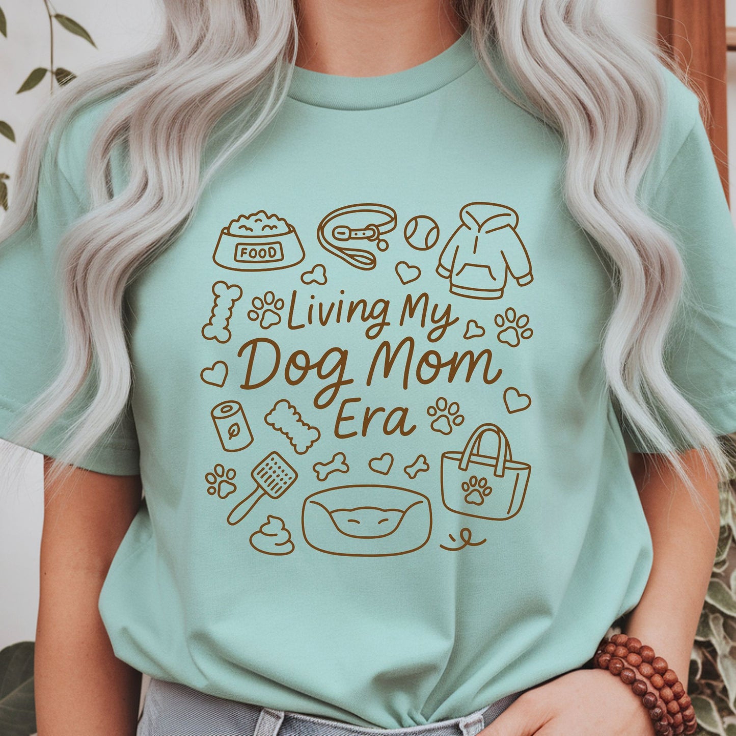 Minimalist dog mom line art design featuring pet essentials including food bowl, leash, hoodie, tennis ball, dog bed, tote bag, bones, and paw prints with Living My Dog Mom Era quote.
