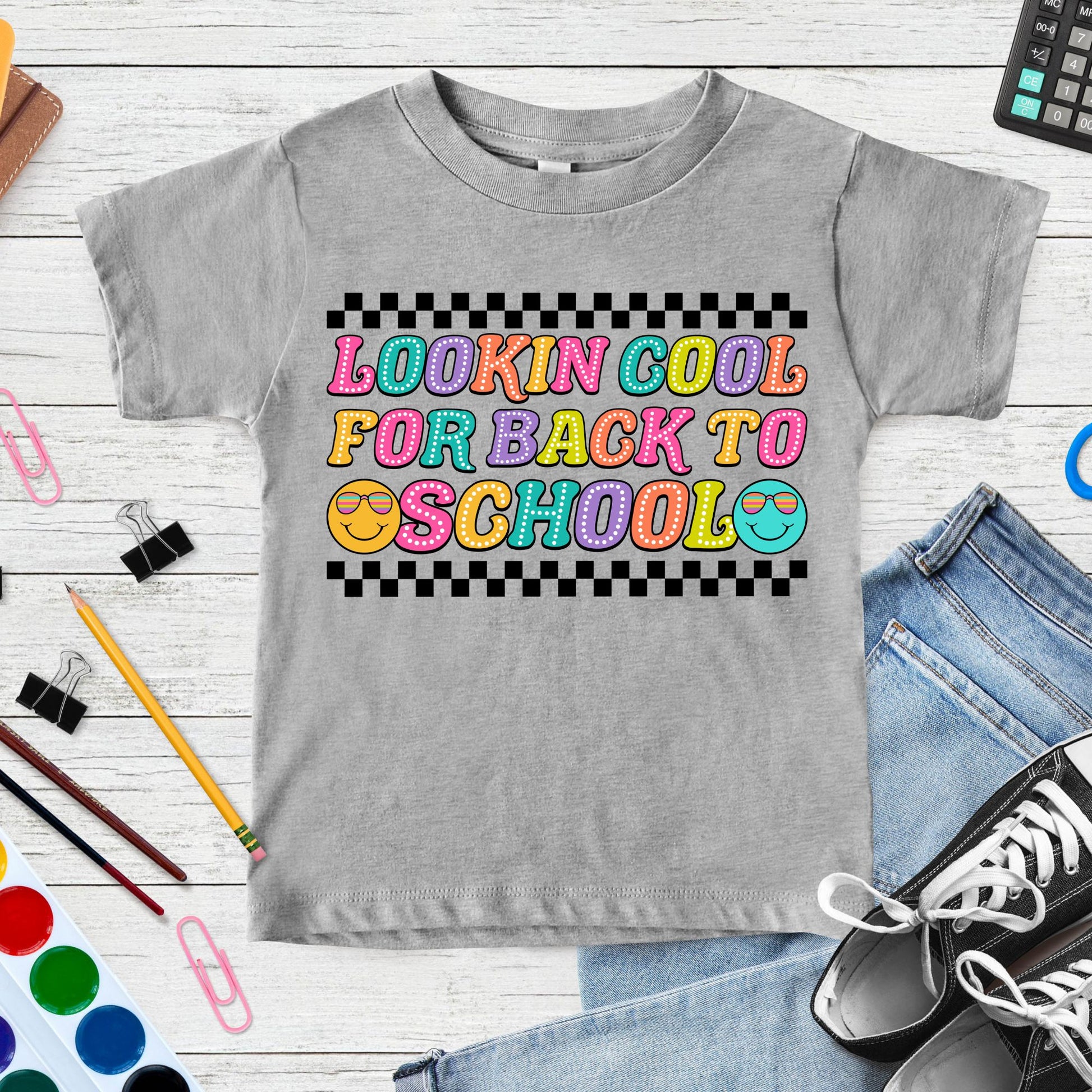 Lookin’ Cool for Back to School design featuring colorful retro bubble letters, two sunglasses smiley faces, and bold black checkerboard accents for toddler, kids, and youth shirts.