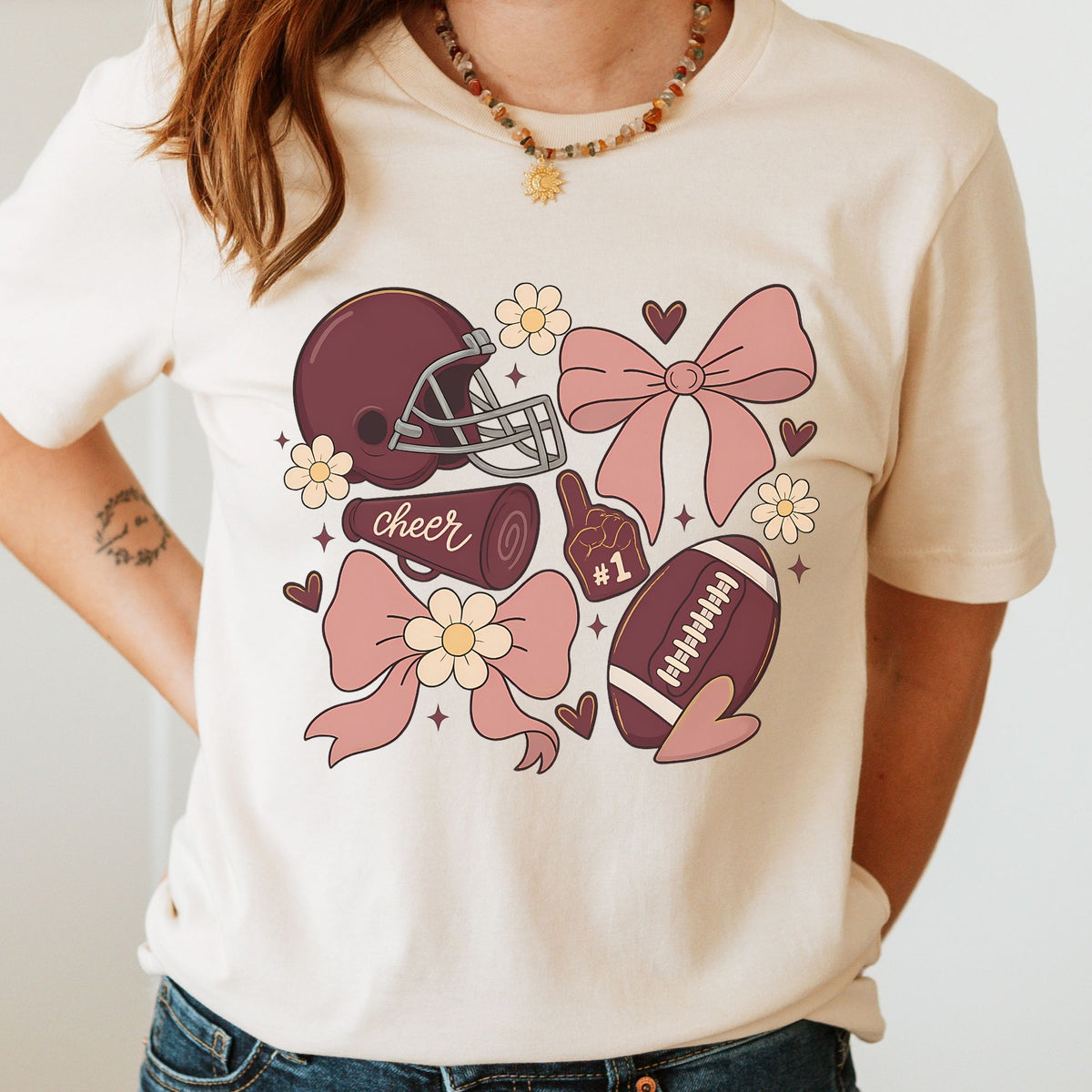 Maroon football cheer bow DTF transfer featuring a maroon football helmet, football, cheer megaphone, foam finger, pink coquette bows, hearts, flowers, and sparkle accents for cheer shirts, football season apparel, and game day sweatshirts.