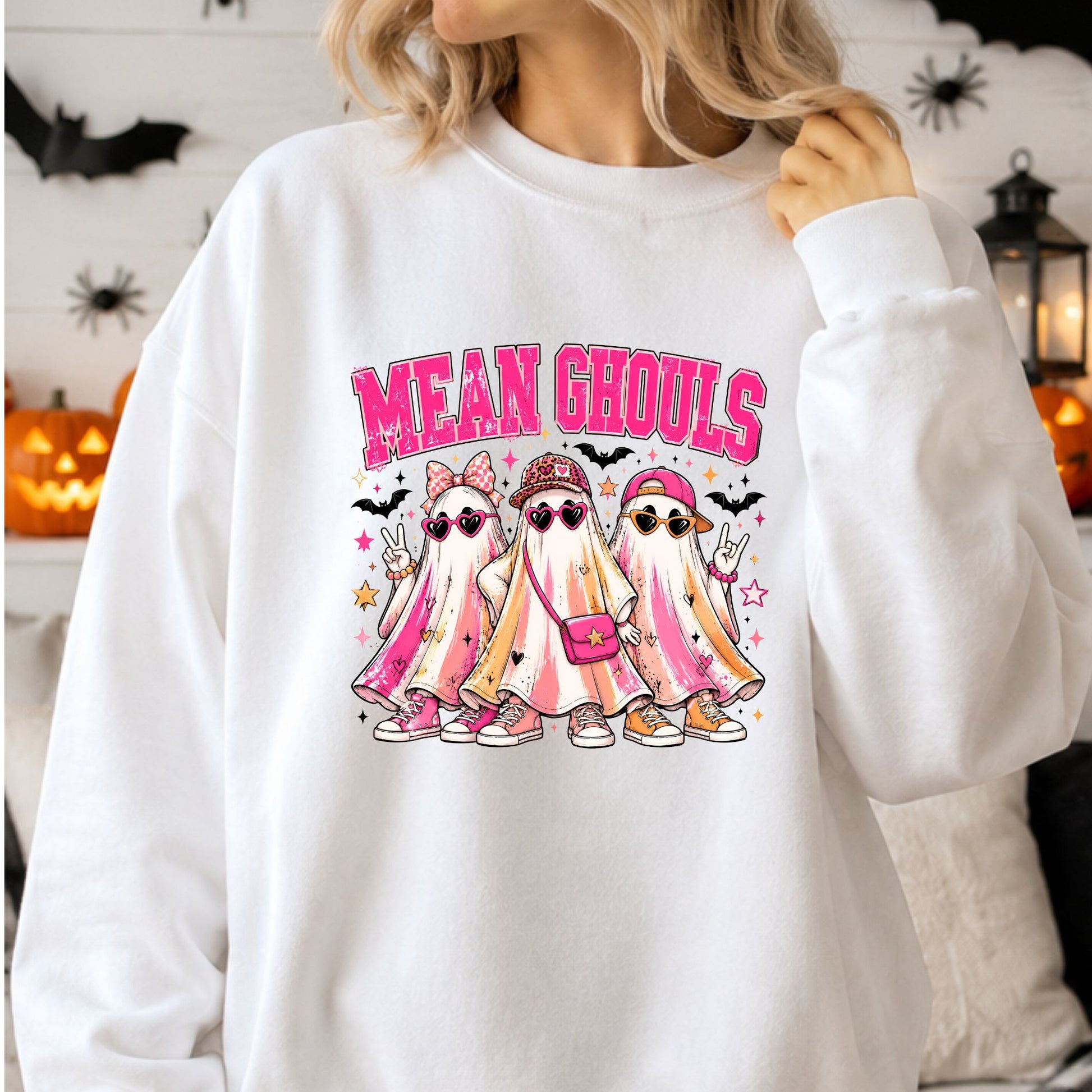 Mean Ghouls Halloween DTF transfer featuring three stylish sheet ghosts wearing heart-shaped sunglasses, colorful hats and sneakers, with a pink crossbody purse, peace signs, bats, stars and bright retro accents on a white sweatshirt mockup.