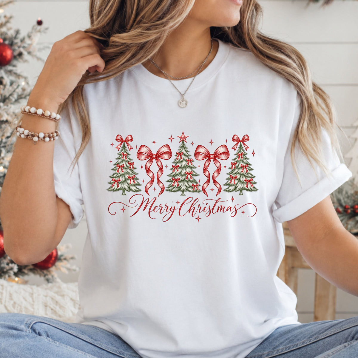 “Merry Christmas” in red script beneath three snowy green trees decorated with red bows, two oversized ribbon bows, a red star topper and red sparkles.