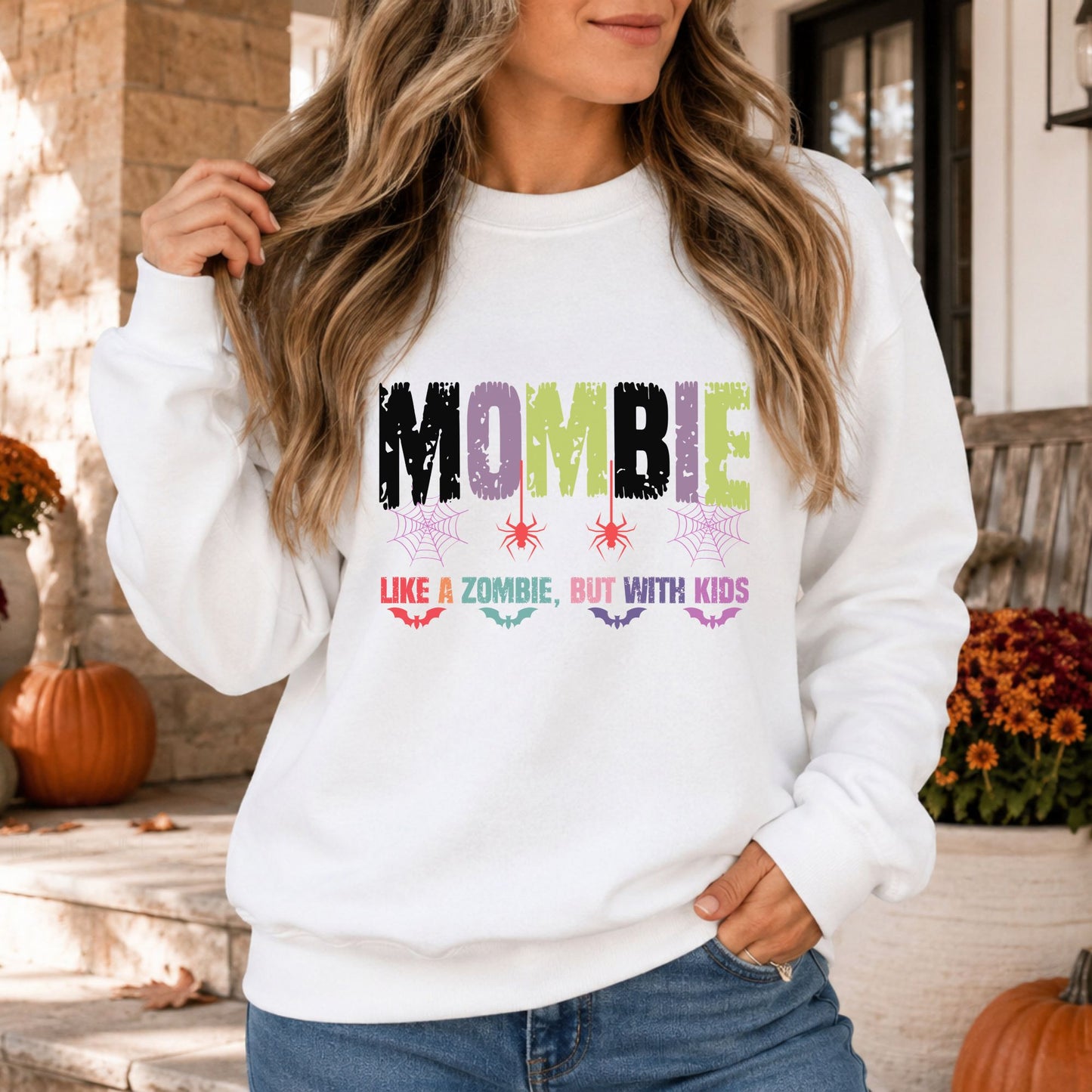 Mombie Like a Zombie but with Kids Halloween DTF transfer featuring distressed black, purple and green lettering with colorful spiders, spiderwebs and flying bats on a white sweatshirt mockup.
