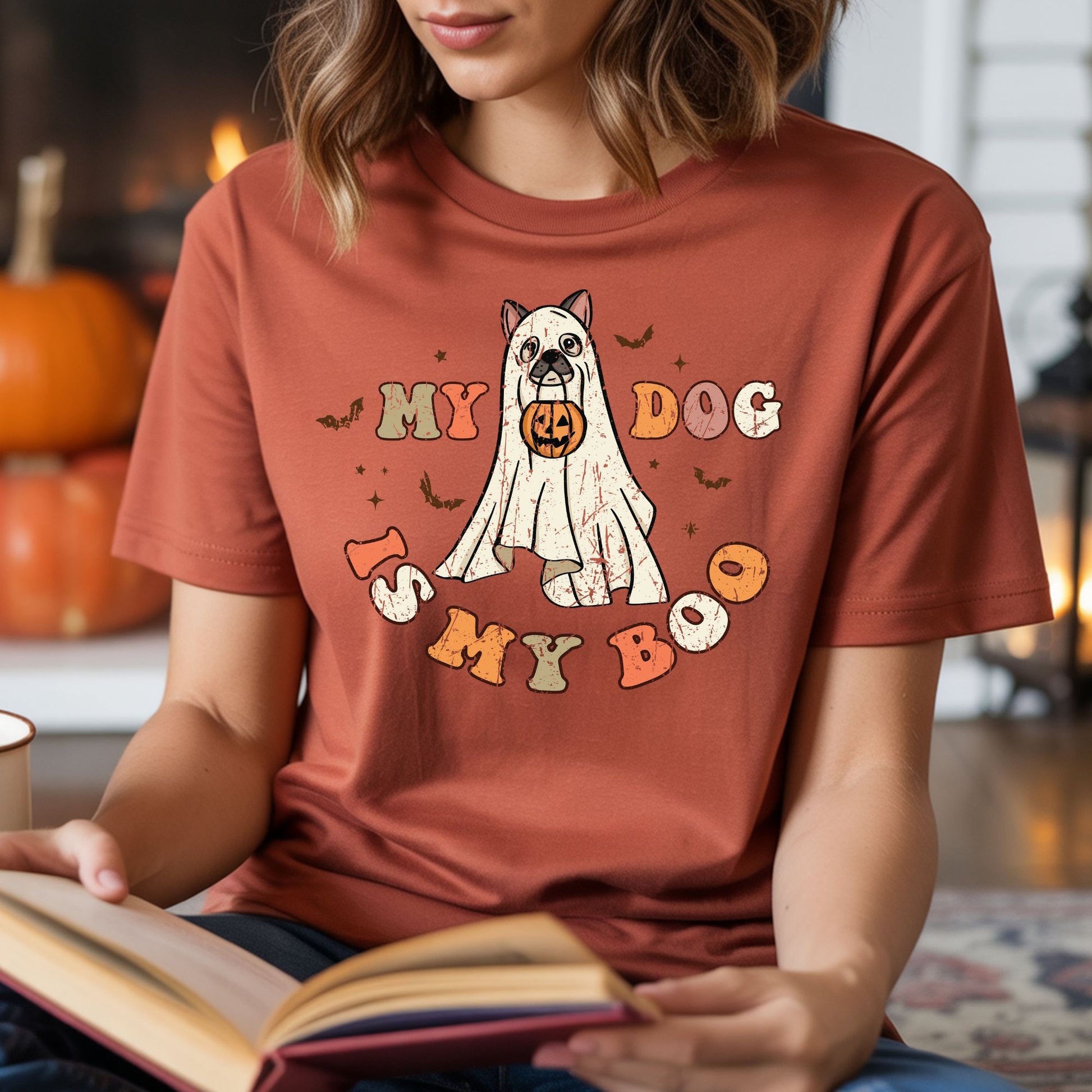 My Dog Is My Boo Halloween DTF transfer featuring a cute dog dressed in a distressed white sheet ghost costume while holding a jack-o’-lantern bucket, surrounded by bats, bones, stars and retro orange lettering on a rust-colored T-shirt mockup.