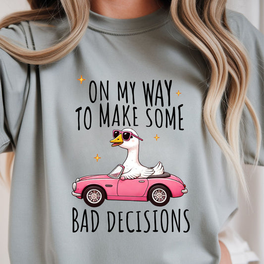 Funny graphic featuring a goose wearing sunglasses driving a pink convertible with the phrase "On My Way to Make Some Bad Decisions." Perfect for sarcastic graphic tees, road trip outfits, and quirky boutique apparel.
