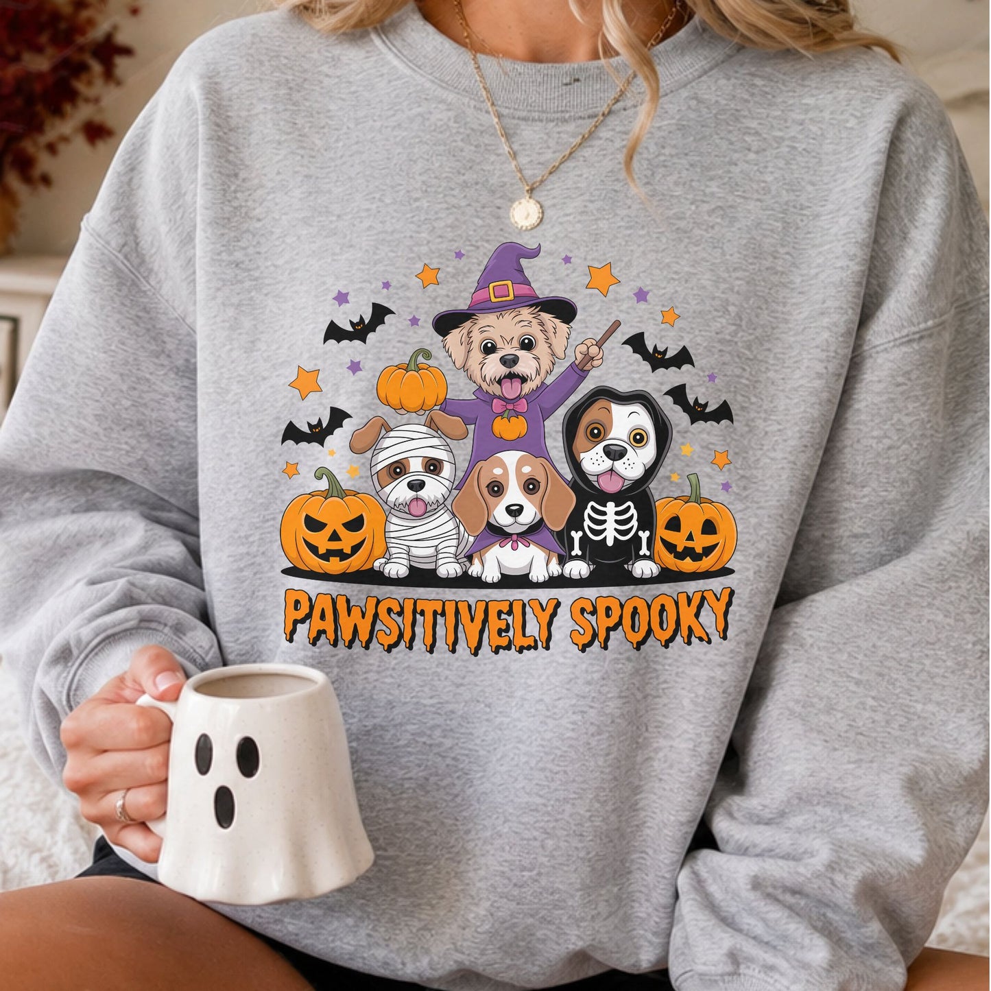 Pawsitively Spooky Halloween DTF transfer featuring four cute dogs dressed in witch, mummy, vampire and skeleton costumes, surrounded by jack-o’-lanterns, flying bats and orange and purple stars on a gray sweatshirt mockup.