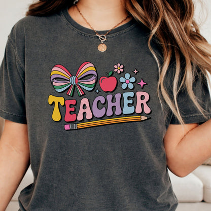 Cute preppy teacher design featuring a colorful striped bow, apple, flowers, pencil, and pastel teacher lettering. Available as a ready-to-press DTF transfer or professionally pressed teacher tee, shirt, sweatshirt, or hoodie. Perfect for back to school, classroom outfits, teacher appreciation gifts, and everyday teacher apparel.