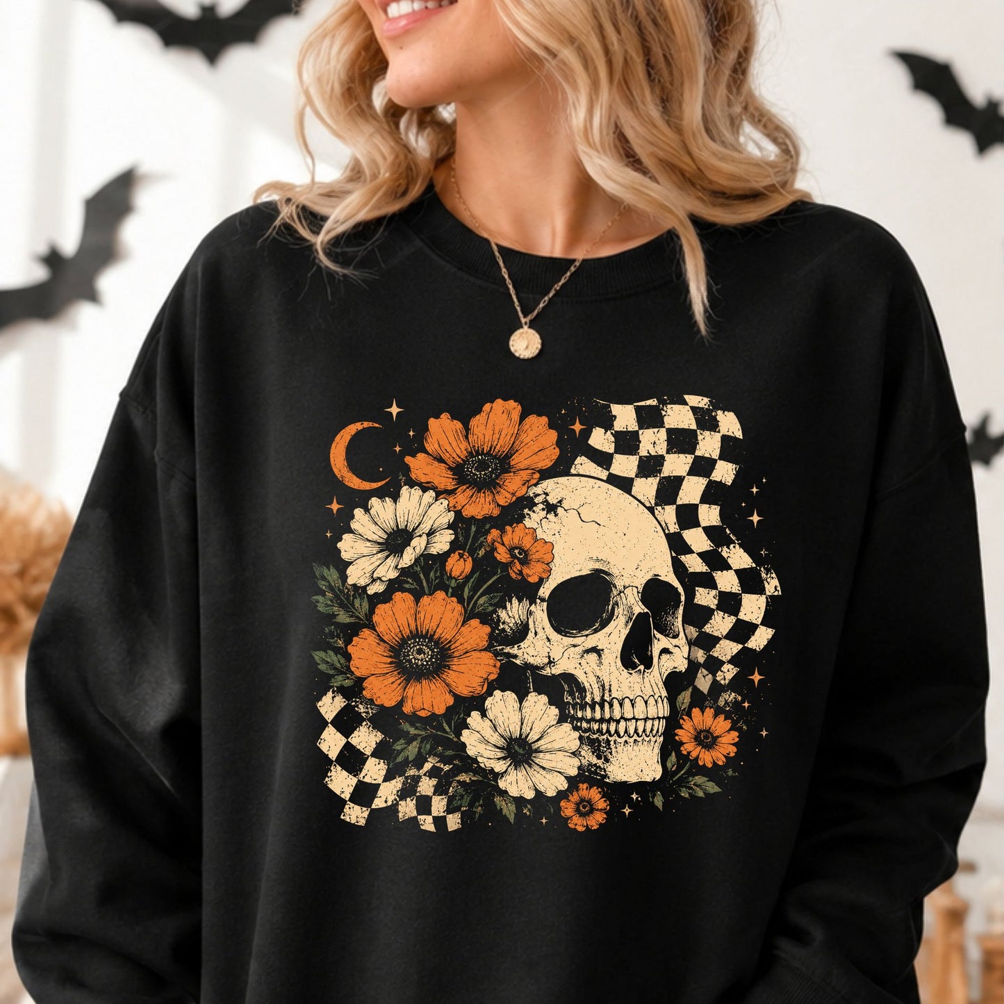 Retro floral skull Halloween DTF transfer featuring a distressed ivory skull surrounded by orange and cream flowers, dark green leaves, a crescent moon, sparkling stars and wavy black-and-cream checkerboard accents on a black sweatshirt mockup.