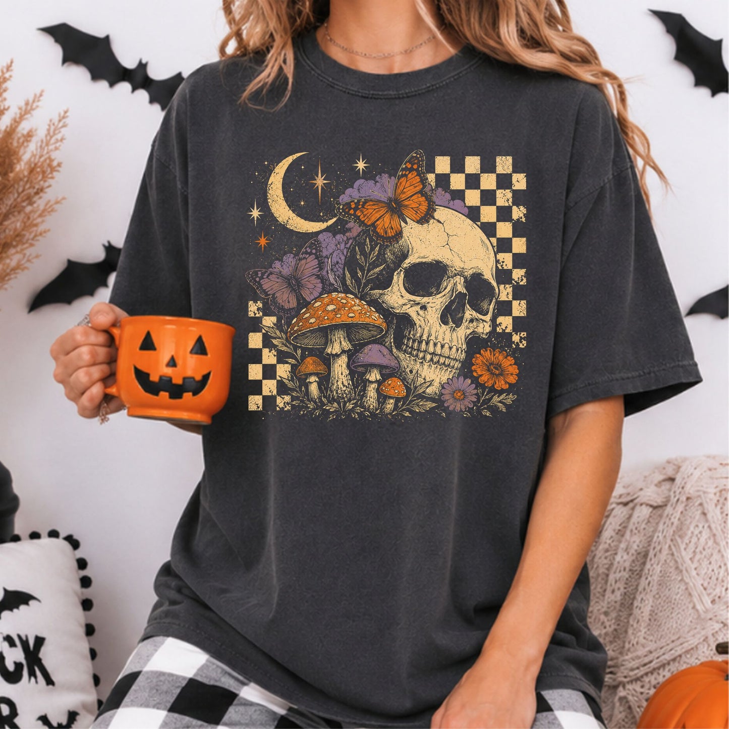 Retro Halloween DTF transfer featuring a distressed ivory skull surrounded by orange and purple butterflies, colorful mushrooms, flowers, leafy accents, a crescent moon, sparkling stars and cream checkerboard details on a dark charcoal T-shirt mockup.