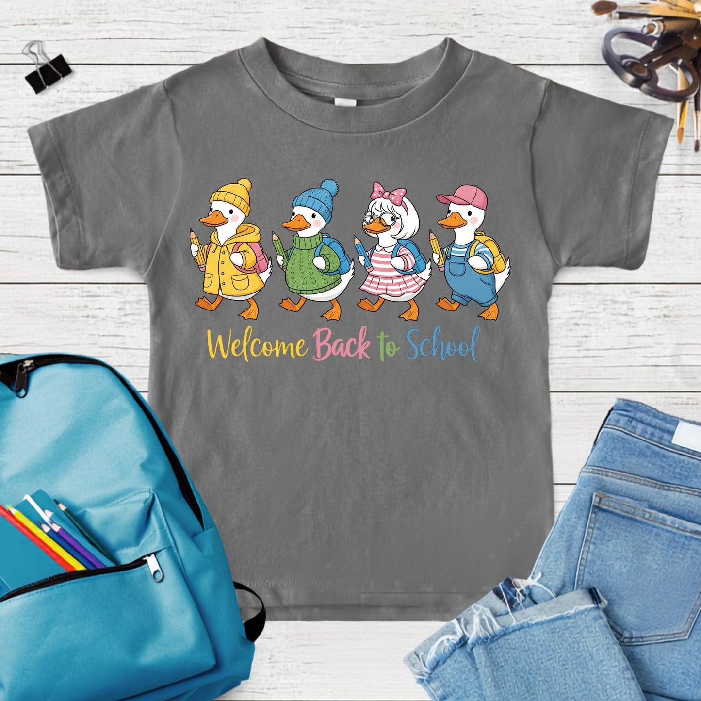 Welcome Back to School design featuring four cute geese in colorful outfits with backpacks and pencils, perfect for first day of school shirts for kids.