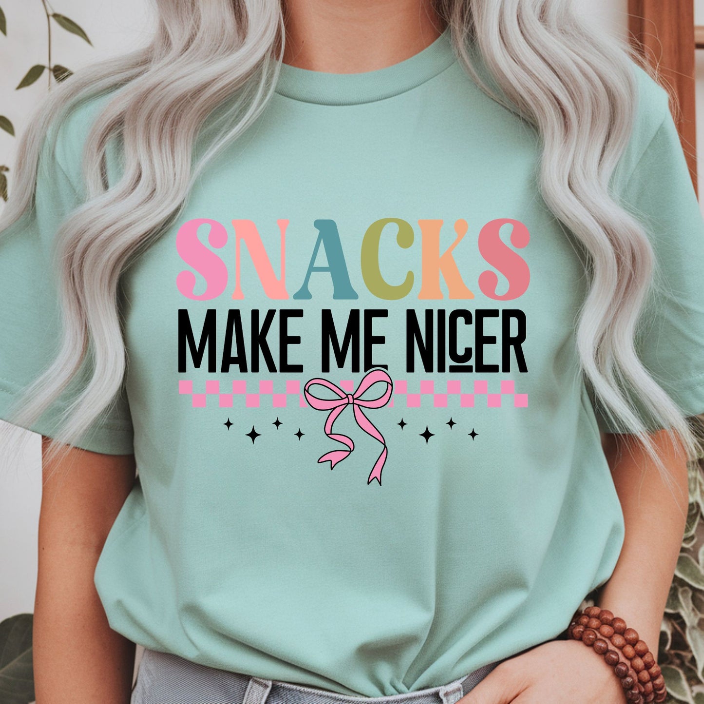 Funny Snacks Make Me Nicer typography featuring colorful retro lettering, pink checkerboard accents, sparkles, and a coquette bow. Perfect for food lovers and snack enthusiasts.
