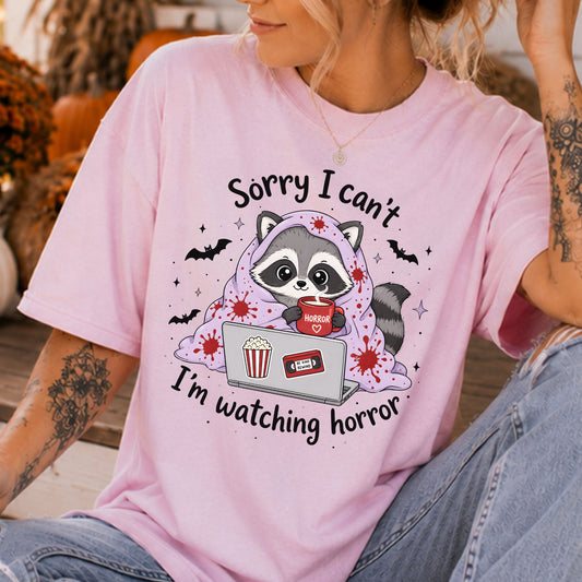 Sorry I Can't I'm Watching Horror Halloween DTF transfer featuring a cute raccoon wrapped in a blood-splattered purple blanket with a Horror mug, laptop, popcorn, VHS tape, and bats.