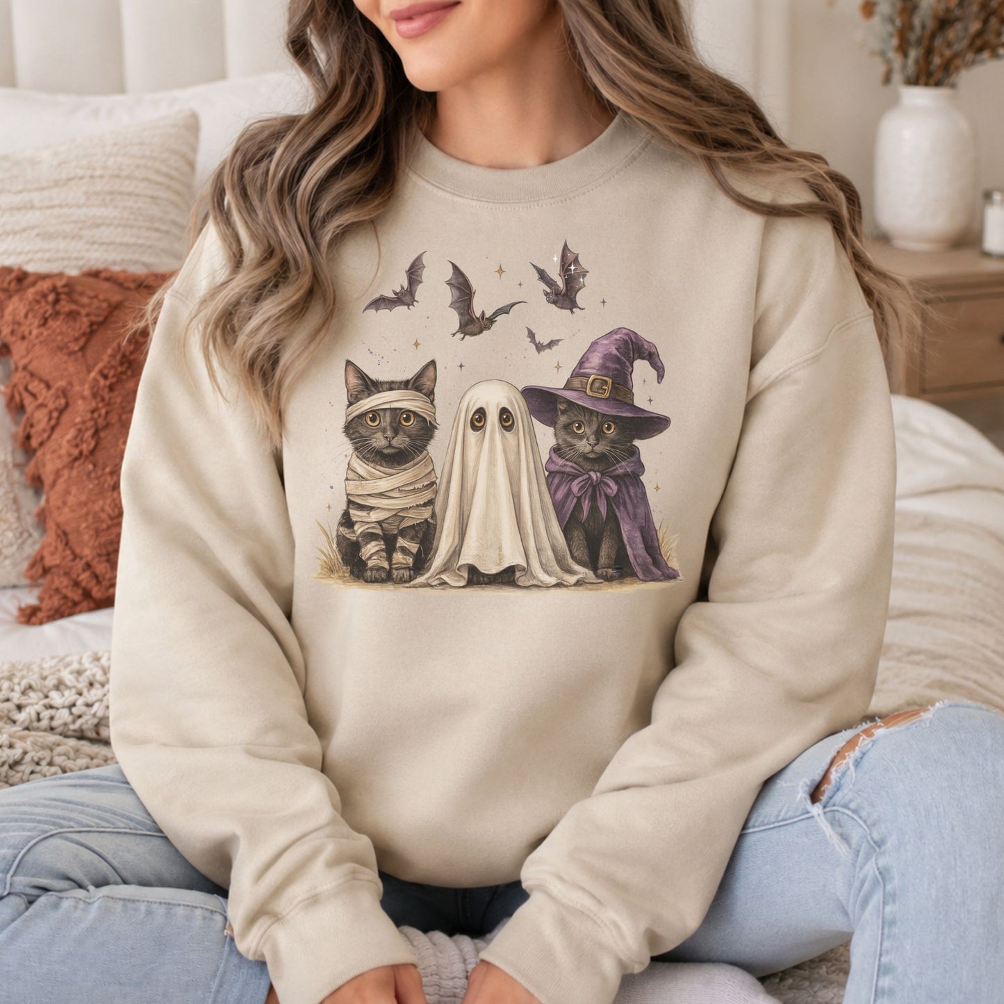 Cream sweatshirt mockup featuring a spooky Halloween trio with a mummy cat, a ghost, and a witch cat with bats overhead.