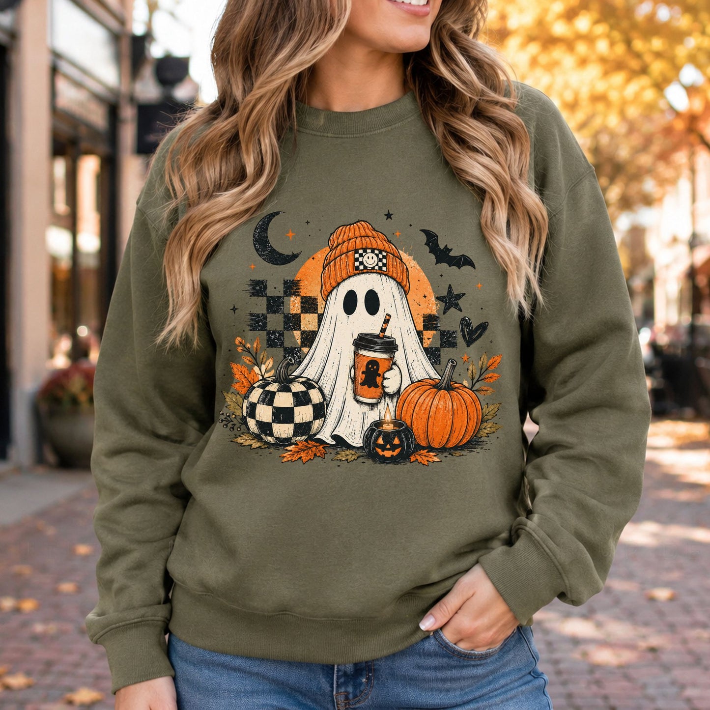 Olive green sweatshirt mockup featuring a spooky ghost holding coffee with checkered pumpkins, orange fall leaves, and Halloween details.