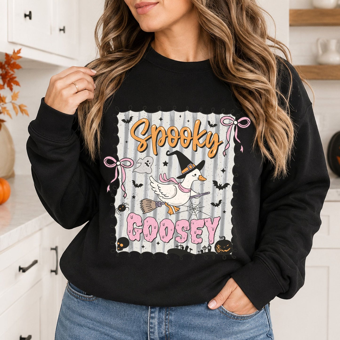 Black sweatshirt mockup featuring a coquette Halloween goose flying on a broom with a witch hat, pink bows, bats, and the phrase Spooky Goosey.