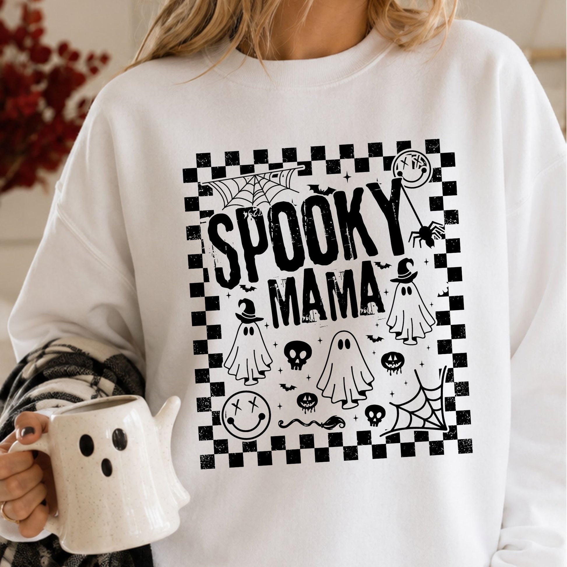 Spooky Mama Halloween DTF transfer featuring bold distressed black lettering surrounded by sheet ghosts, skulls, bats, spiders, spiderwebs, spooky smiley faces and a black-and-white checkerboard border on a white sweatshirt mockup.