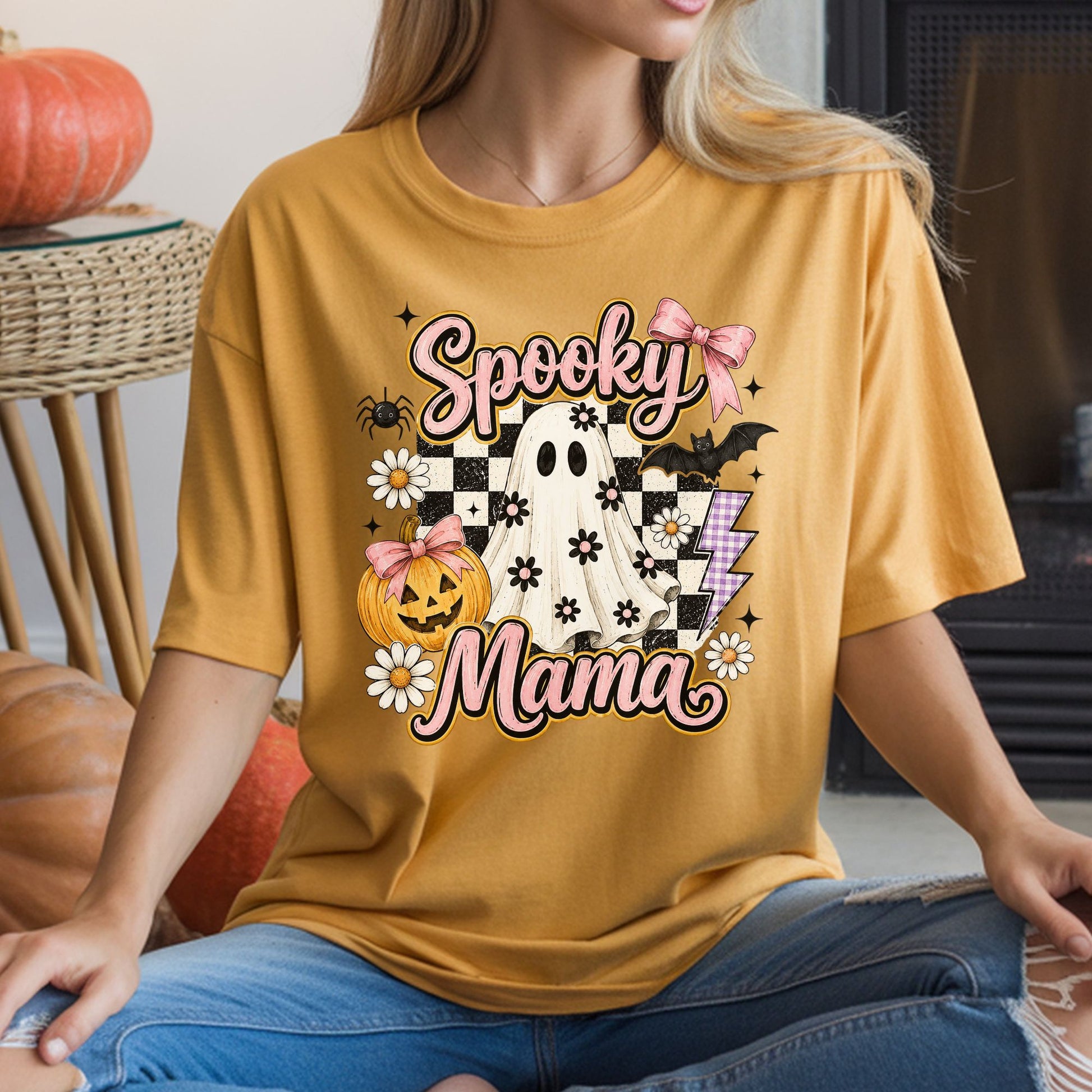 Spooky Mama Halloween DTF transfer featuring a floral sheet ghost with pink bows, a bow-topped jack-o’-lantern, daisies, a bat, spider, purple lightning bolt and distressed black-and-white checkerboard accents on a mustard yellow T-shirt mockup.
