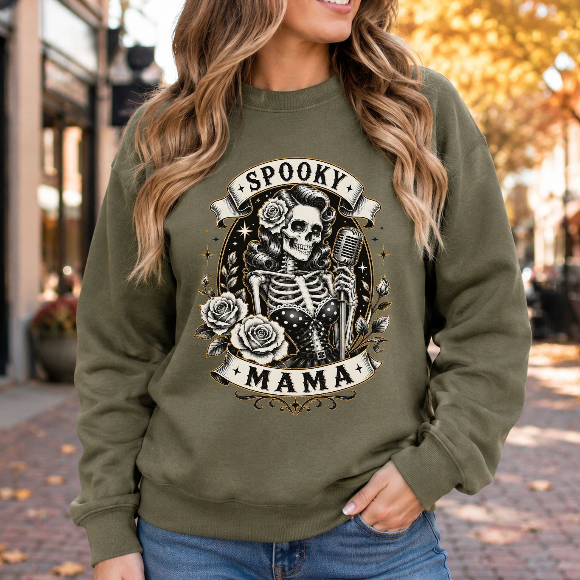 Spooky Mama Halloween DTF transfer featuring a glamorous retro skeleton singer holding a vintage microphone, wearing a polka-dot corset and flower in her curled hair, surrounded by roses, stars and decorative banner accents on an olive green sweatshirt mockup.