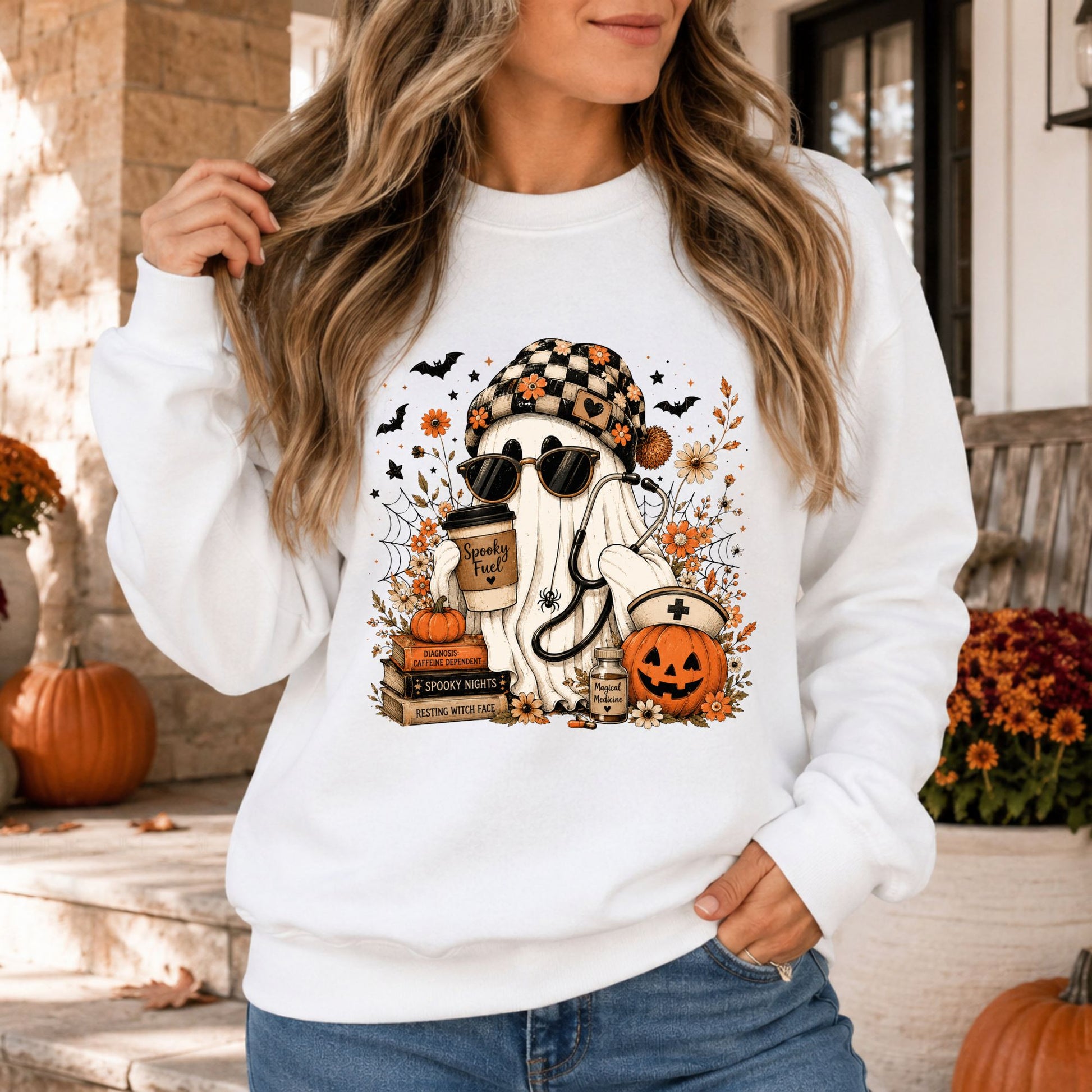 Spooky nurse Halloween DTF transfer featuring a sheet ghost wearing sunglasses and a checkered beanie while holding a Spooky Fuel coffee cup and stethoscope, surrounded by a nurse pumpkin, medicine bottle, stacked books, orange flowers, bats, spiderwebs and fall accents on a white sweatshirt mockup.
