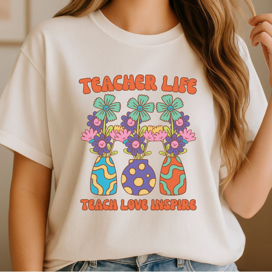 Teacher Life Teach Love Inspire design featuring three colorful retro flower vases filled with smiling daisies and bold orange classroom lettering for teacher shirts and school apparel.
