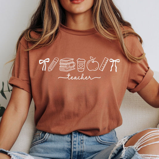 Minimal white Teacher Vibes design featuring school doodles including bows, pencil, books, coffee cup, apple, and ruler on a rust-colored shirt.
