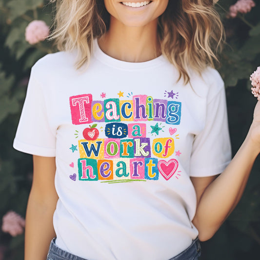 Teaching Is a Work of Heart teacher design featuring bright multicolor block lettering, an apple, hearts, stars, and playful classroom accents for teacher shirts and school apparel.