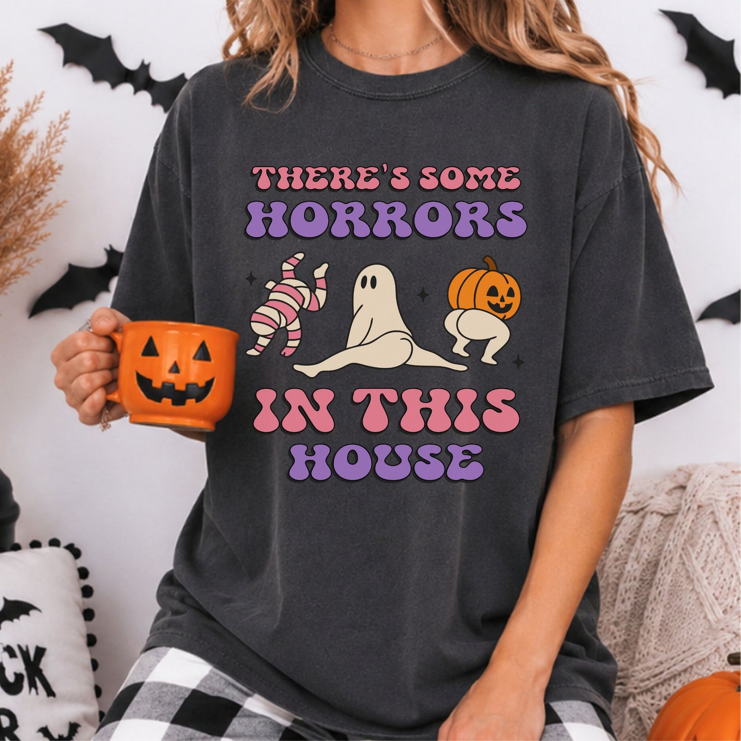 There’s Some Horrors in This House Halloween DTF transfer featuring a pink-striped mummy, sheet ghost doing the splits and pumpkin-headed character posing playfully beneath retro pink and purple lettering on a dark charcoal T-shirt mockup.