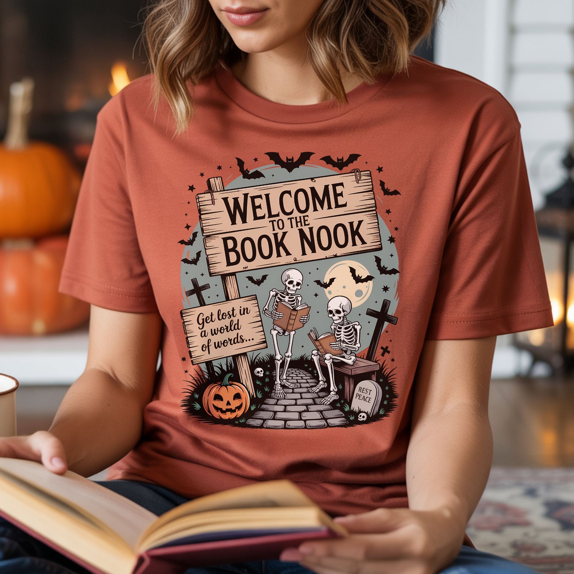 Rust-colored T-shirt mockup featuring two skeletons reading books with the phrase Welcome to the Book Nook, plus a pumpkin, bats, and spooky graveyard details.
