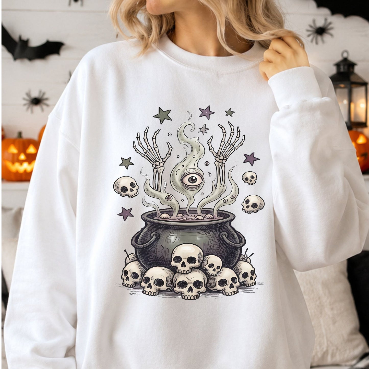 Gothic Halloween DTF transfer featuring a dark witch cauldron surrounded by skulls, with eerie green smoke forming a large mystical eye, raised skeleton hands, floating skulls and muted purple and green stars on a white sweatshirt mockup.
