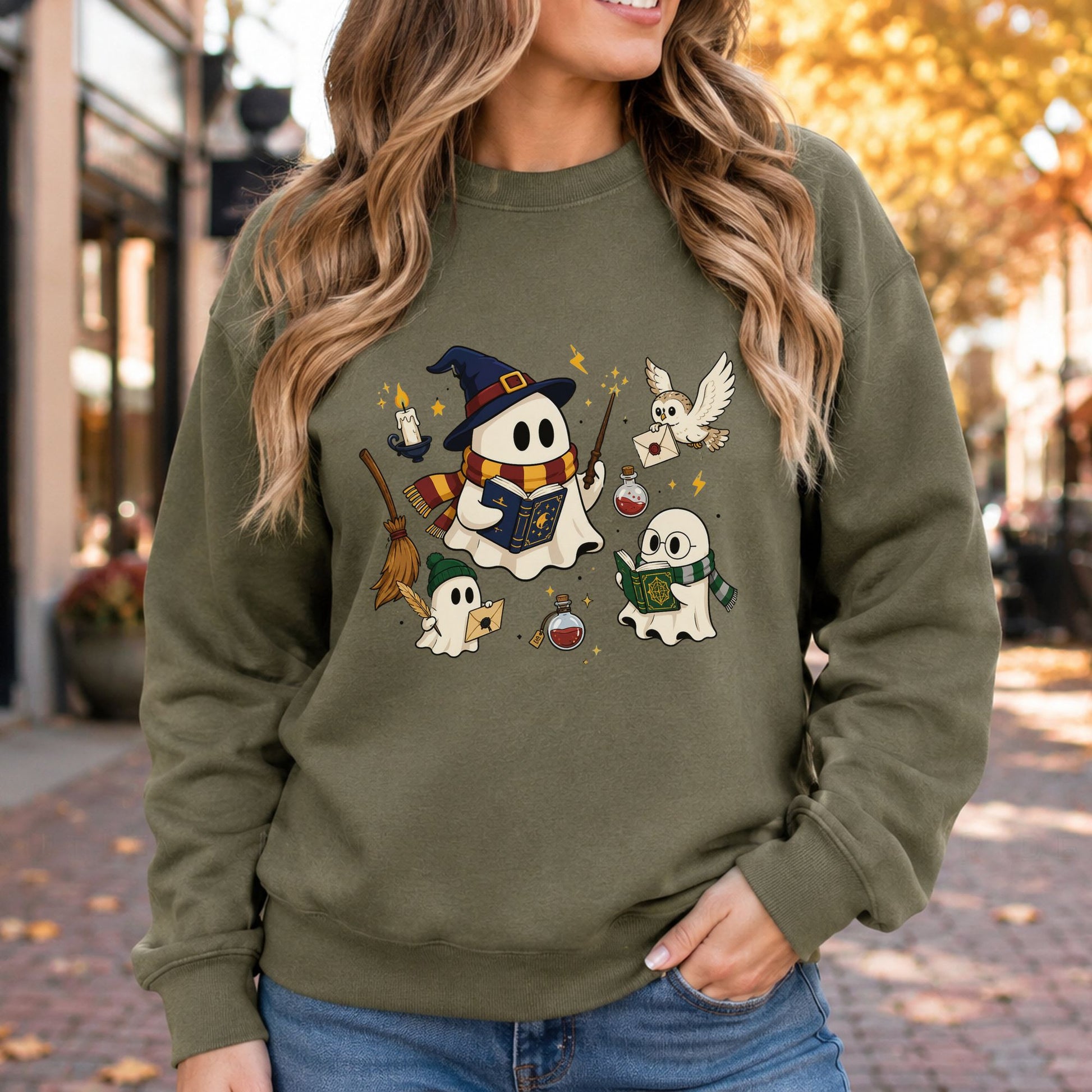 Magical Halloween DTF transfer featuring three sheet ghosts dressed as wizard students with colorful scarves, spell books and a wand, surrounded by an owl carrying a letter, broomstick, floating candle, potion bottles, lightning bolts and sparkling stars on an olive green sweatshirt mockup.